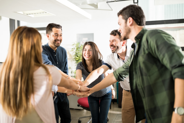 Equipo celebrando en oficina con manos unidas.
